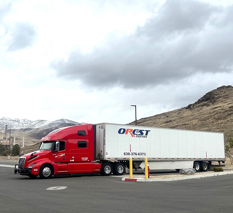 A red OREST Express tractor-trailer parked at a truck stop in the mountains